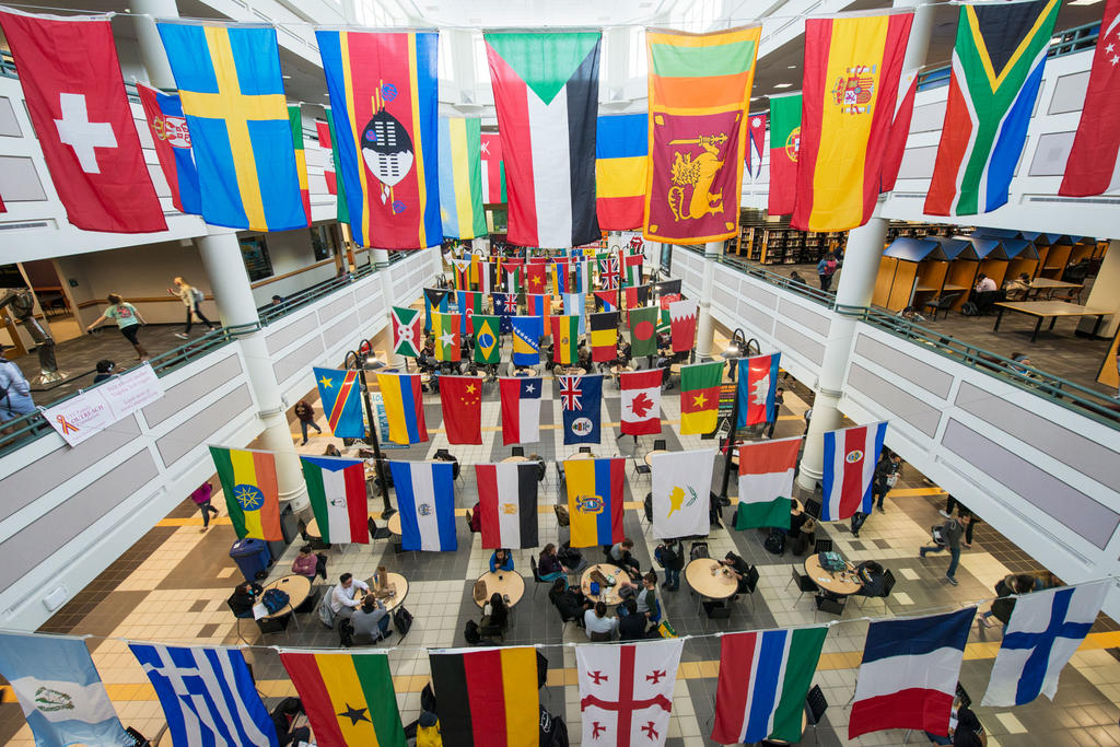 Colorful flags from around the world hang above the Johnson Center with students below at George Mason University