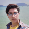 Tazeem Ahmad, IST PhD student at Mason, takes picture by the ocean and wears a plaid shirt, yellow t-shirt, and glasses.